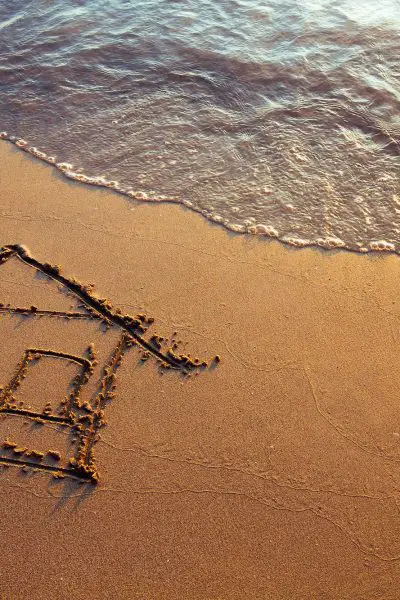 Drawing of a simple house in the sand with water lapping nearby