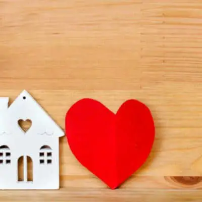 What is a homemaker? Small cutout house with red heart on wooden background