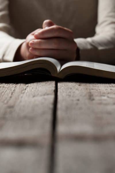 Woman hands praying with a bible in a dark over wooden table